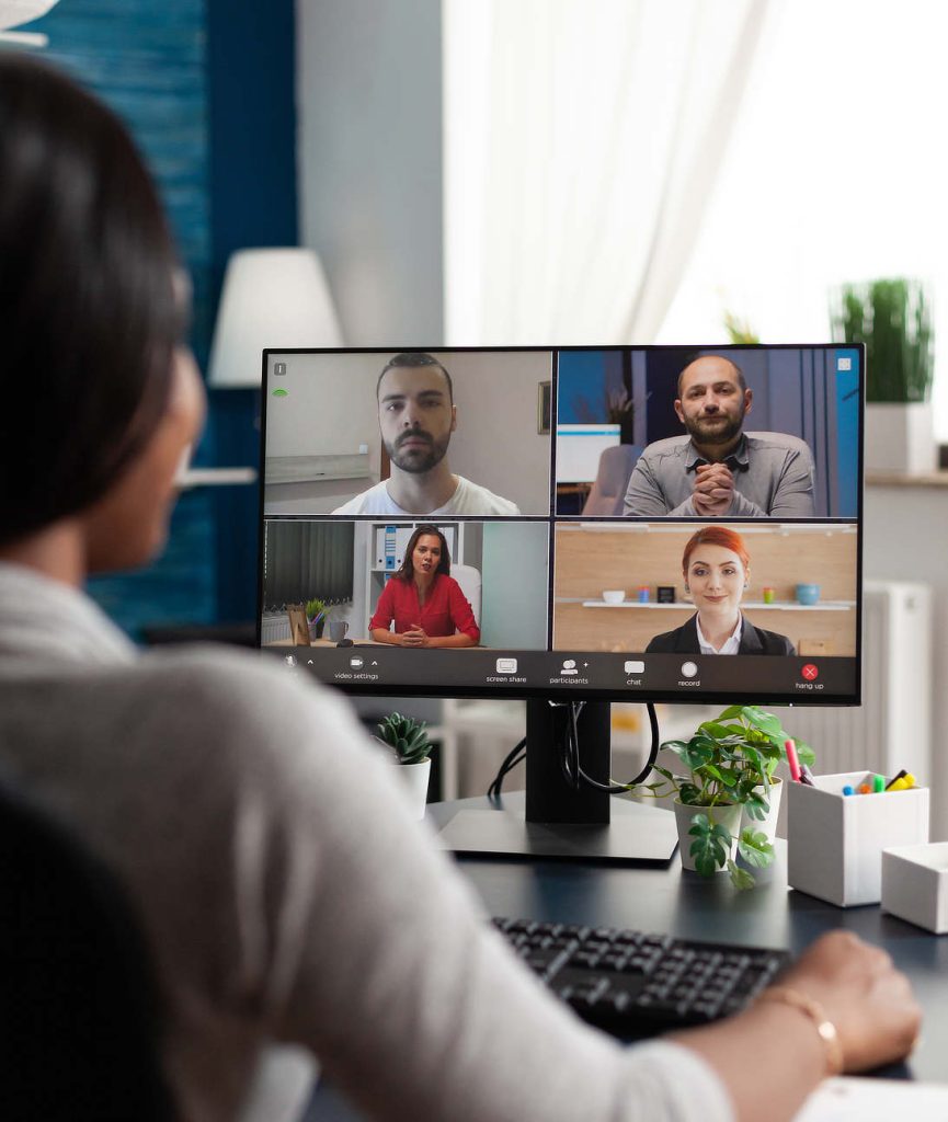 A woman participating in a virtual meeting with four colleagues displayed on her computer screen, symbolizing remote team collaboration.