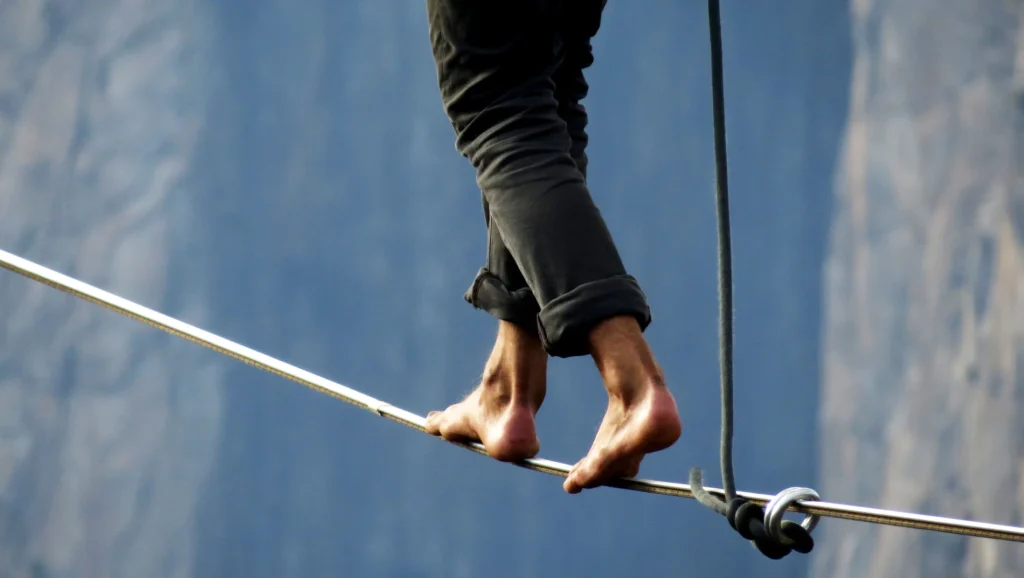 Barefoot person walking a tightrope, symbolizing the delicate balance of leadership and trust in remote teams.