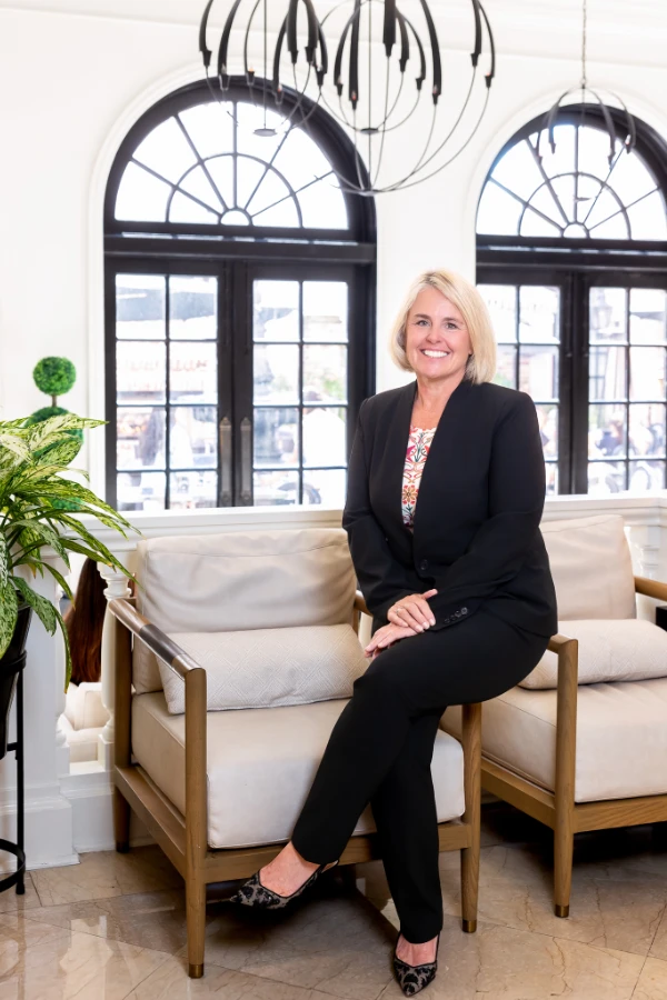 Cecilia Dahl sits poised in a light-filled space with arched windows, smiling and dressed in professional attire.